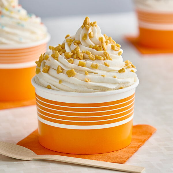 An orange Choice paper cup filled with ice cream topped with whipped cream and sprinkles.