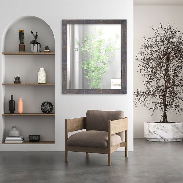 A modern living room with a BrandtWorks Lauralee Industrial Rust Finish Mirror above a wooden chair and a plant in a vase.