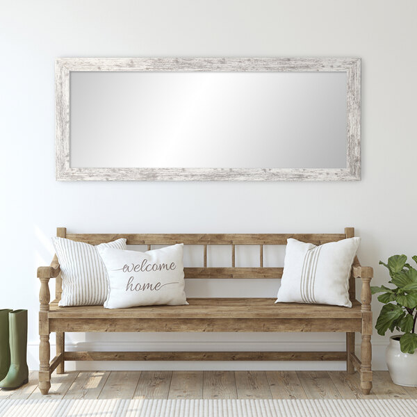 A wooden bench with pillows in front of a white wooden American barn wall mirror.