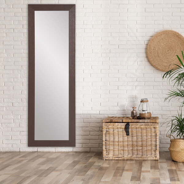 A BrandtWorks modern espresso finish mirror on a wall above a wooden floor with a basket and a plant.