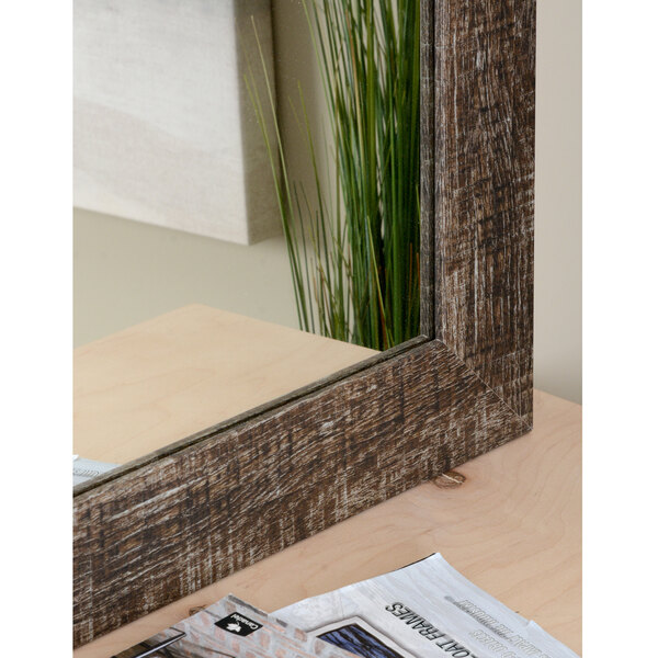 A BrandtWorks Urrutia mirror with a wooden frame on a wood surface with a plant.