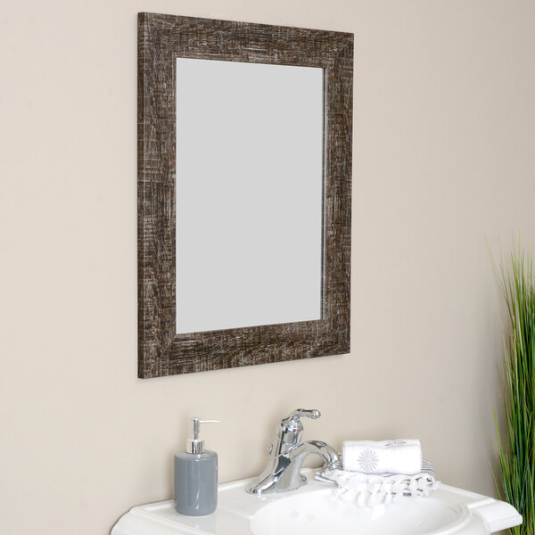 A BrandtWorks Urrutia mirror with a distressed brown finish above a white surface with a silver faucet.
