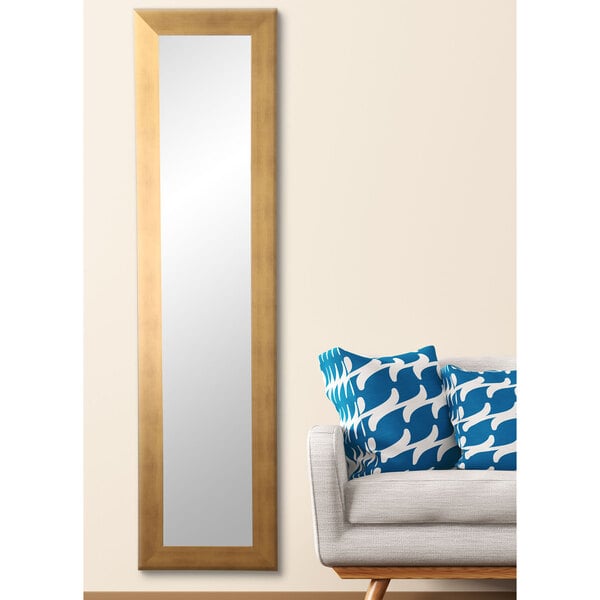 A BrandtWorks long gold mirror hanging on a white wall next to a couch.