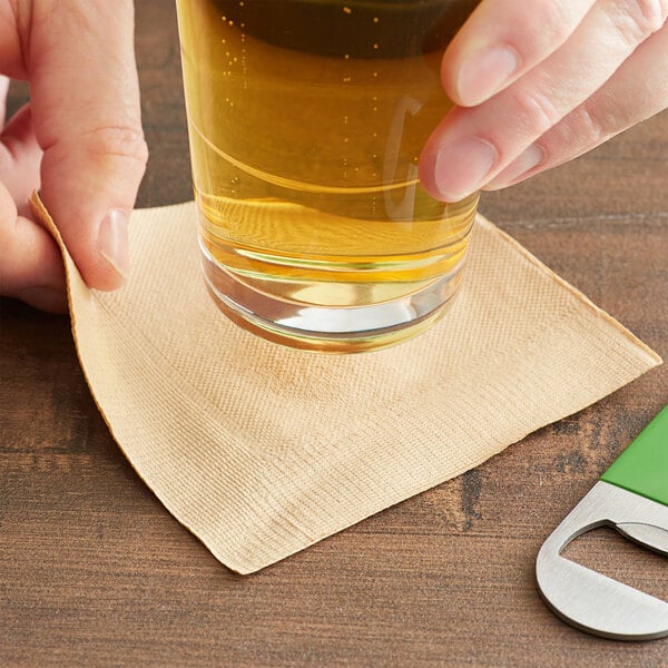 A hand holding a natural kraft beverage napkin wrapped around a glass of beer.