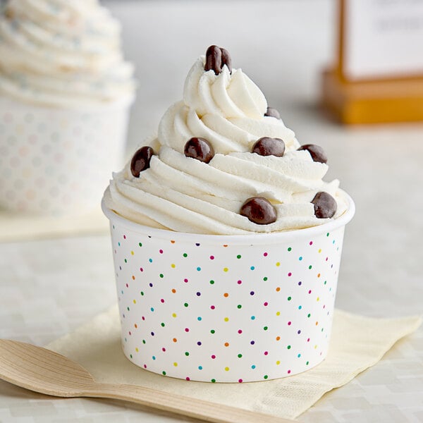 A Choice polka dot paper food cup filled with ice cream with white frosting and colorful dots.