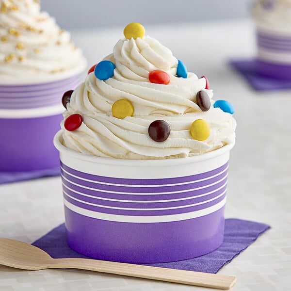 A purple and white paper cup with a scoop of ice cream and candy on top.