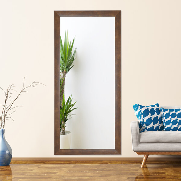 A BrandtWorks mocha walnut brown finish mirror on a wall above a couch with a blue pillow and a blue vase with branches.