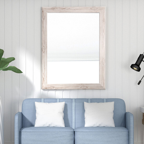 A blue couch with white pillows in front of a cream farmhouse mirror.