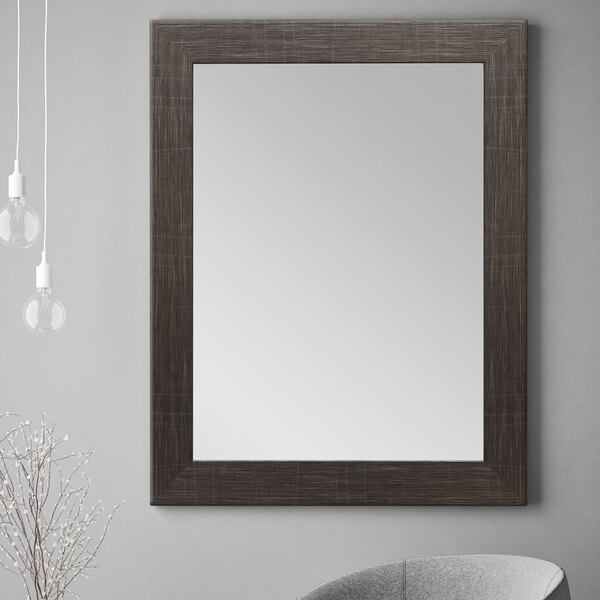A BrandtWorks Scratched Black Finish Mirror on a wall in a room with a grey chair.