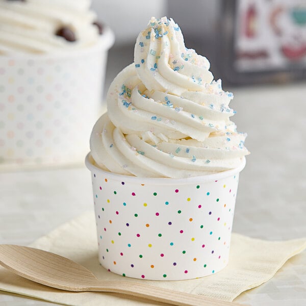 Two white polka dot paper cups filled with frozen yogurt topped with sprinkles.