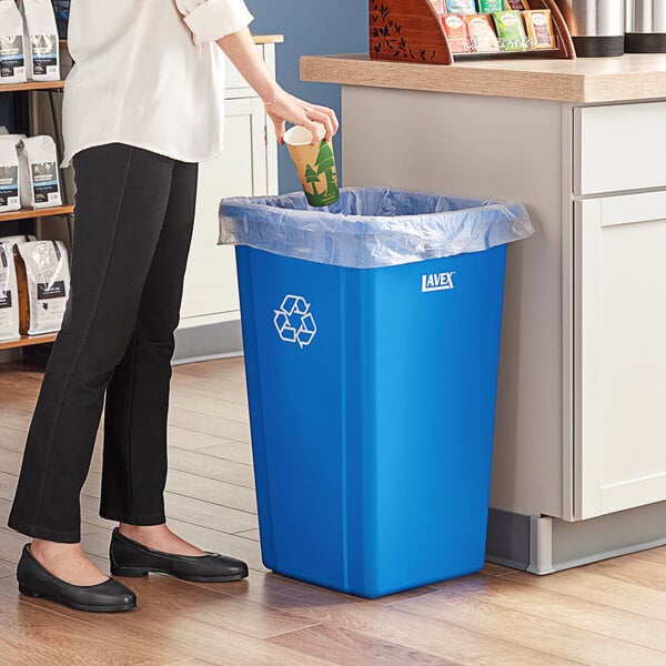 A woman putting a paper cup into a blue Lavex recycling can.