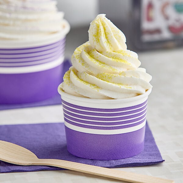 A close-up of 2 purple and white Choice paper frozen yogurt cups with white and yellow frosting.