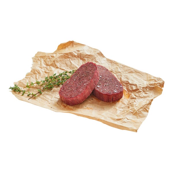 Two plant-based vegan steaks on parchment paper with a sprig of thyme.