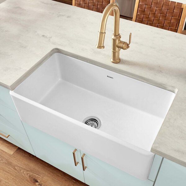 A white Ruvati Fiamma farmhouse sink with a silver sink drain.