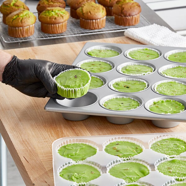 A hand in a black glove holding a green pistachio muffin.