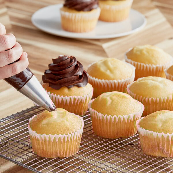 A person using a pastry bag to frost a white cupcake.