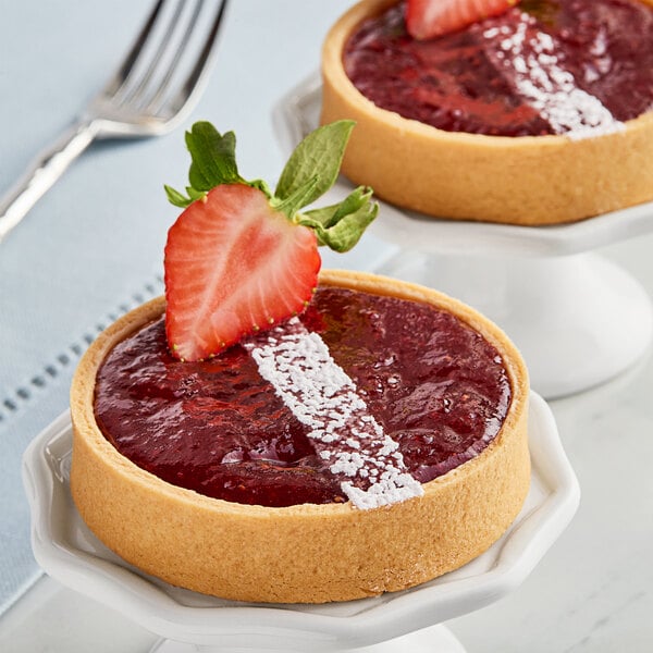 A dessert plate with two small tarts topped with Crofter's Organic Strawberry Preserves and a fork.