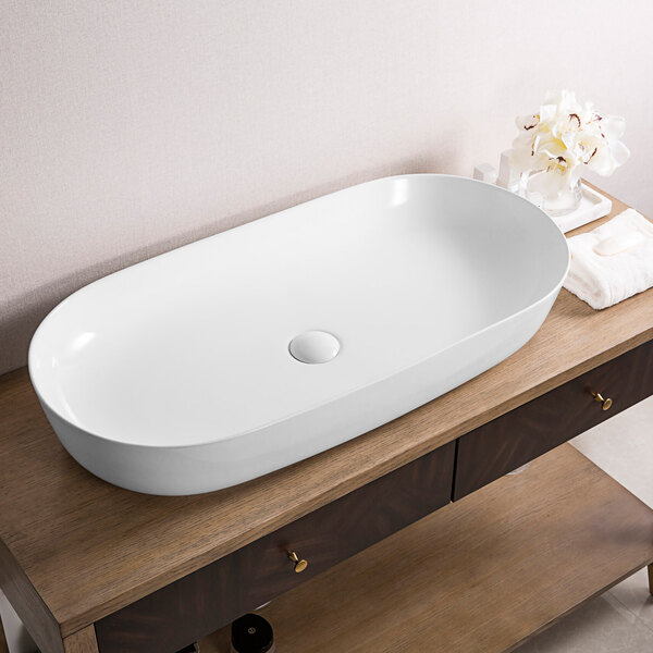 A Ruvati white vitreous porcelain oval vessel sink on a wood table.