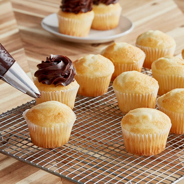 A person using a pastry bag to frost white cupcakes.