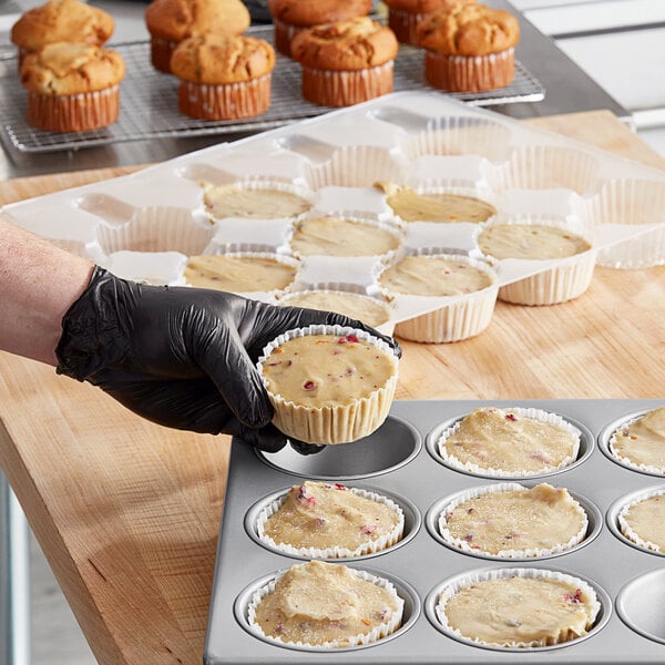 A person in gloves holding a Brill cranberry orange muffin in a muffin tin.