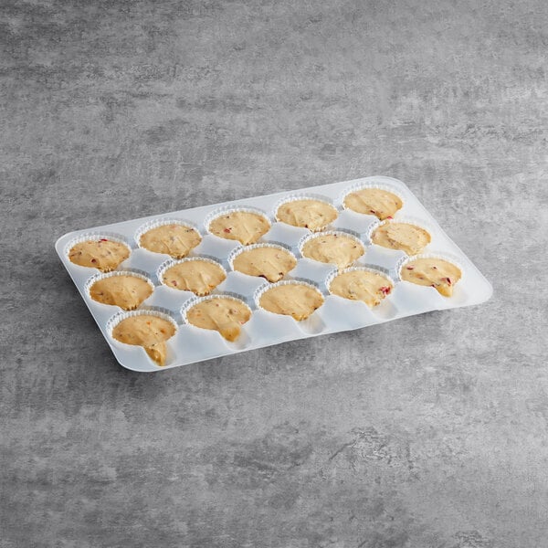 A tray of Brill pre-portioned cranberry orange muffin batter with white paper cups on a concrete surface.