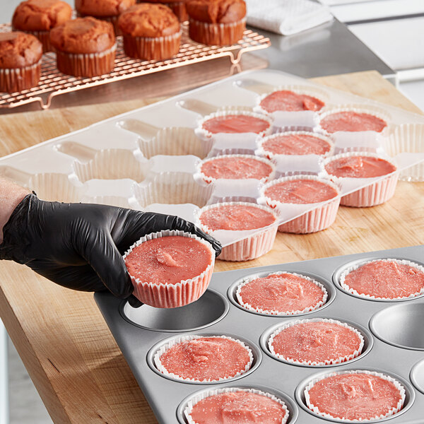 A person in gloves putting Brill strawberry muffin batter into a muffin tin.