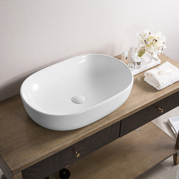 A Ruvati white vitreous porcelain oval vessel sink on a wood table.