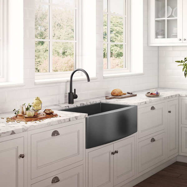 A close up of a Ruvati Terraza farmhouse sink in a kitchen with white cabinets.