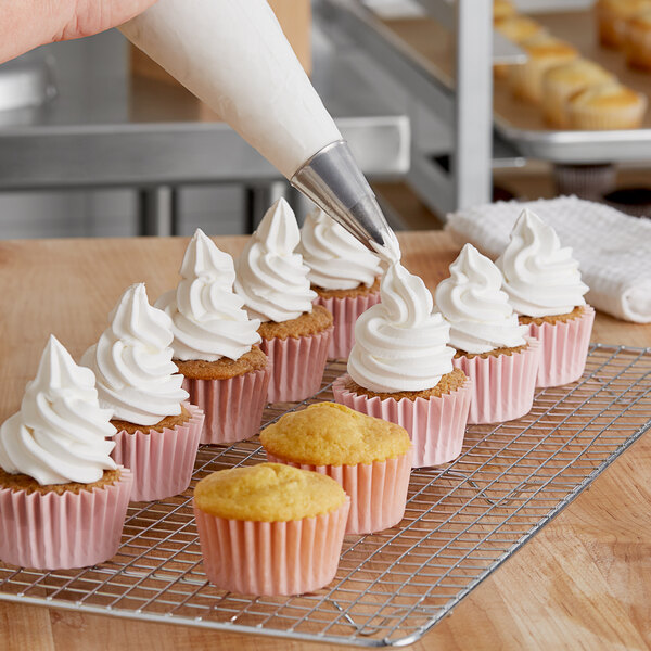 A person using a pastry bag to frost a cupcake with Brill Whipped Vanilla Topping.