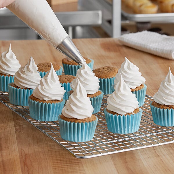 A person using a pastry bag to frost a cupcake with Brill Smooth 'N Silky vanilla topping.