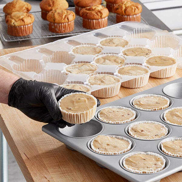 A person in gloves putting Brill banana nut muffin batter into a muffin tin.