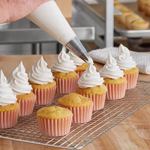 A person using a pastry bag to ice cupcakes with Brill Smooth 'N Silky Whipped Vanilla Topping.