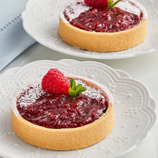 Two small tarts with Crofter's Organic Raspberry Preserves on white plates.