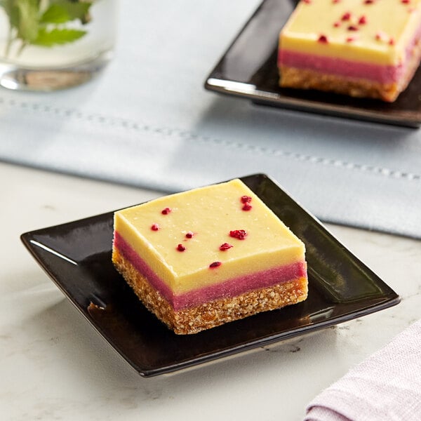 A square Nats Rawline passion fruit and raspberry cake on a black plate.