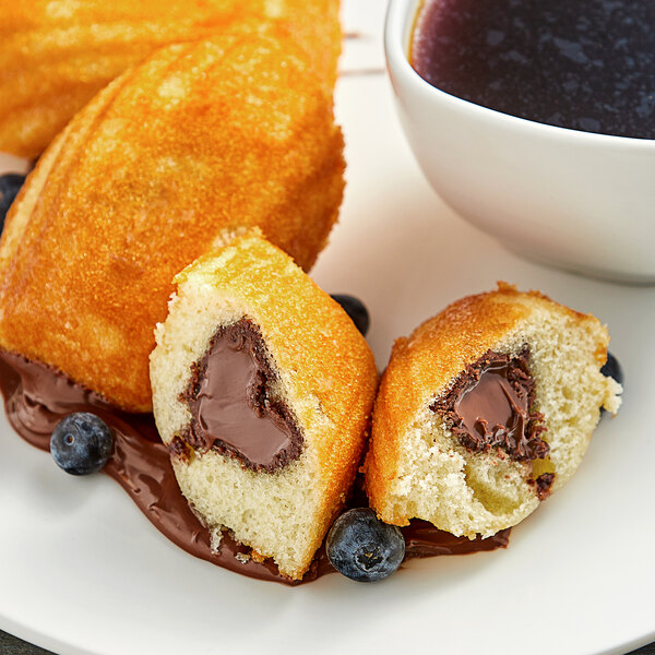 A white plate with a St. Michel Chocolate Hazelnut-Filled Madeleine next to a cup of coffee.