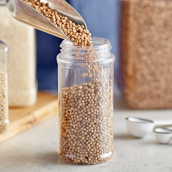 A person pouring brown rice into a round clear plastic spice container.