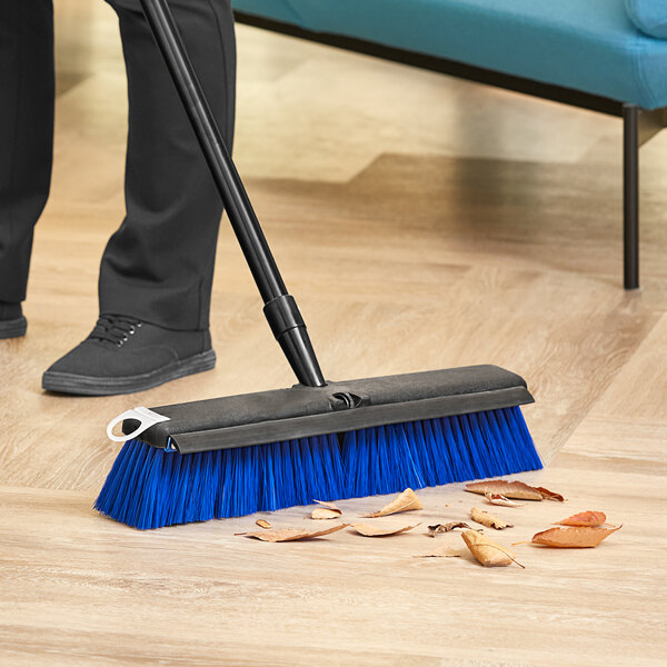 A person using a Lavex push broom with unflagged bristles to sweep the floor.