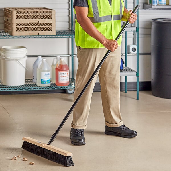 A man in a safety vest sweeping a grocery store aisle with a Lavex wood push broom.