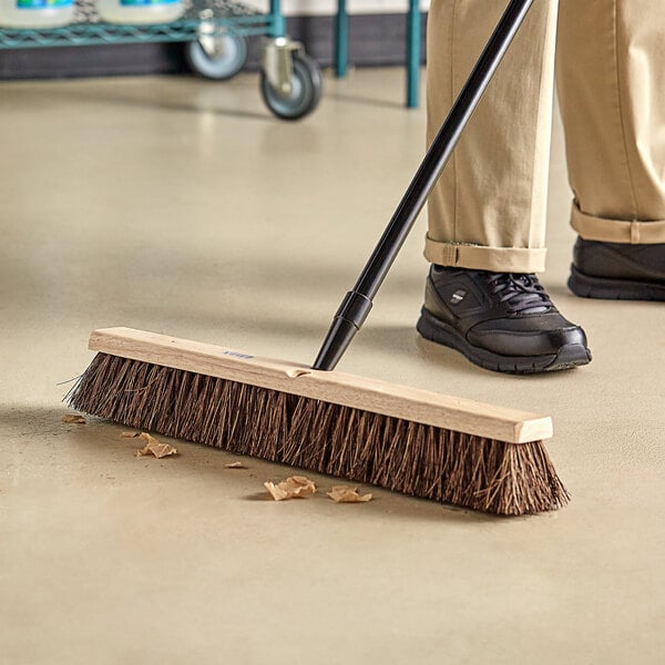 A person sweeping a floor with a Lavex wood push broom head.