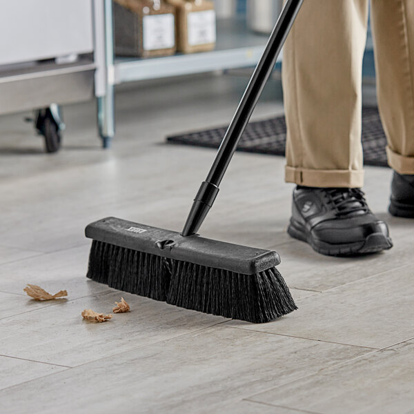 A person sweeping the floor with a Lavex polypropylene push broom head.