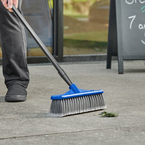 A person sweeping the ground with a Lavex blue push broom head.