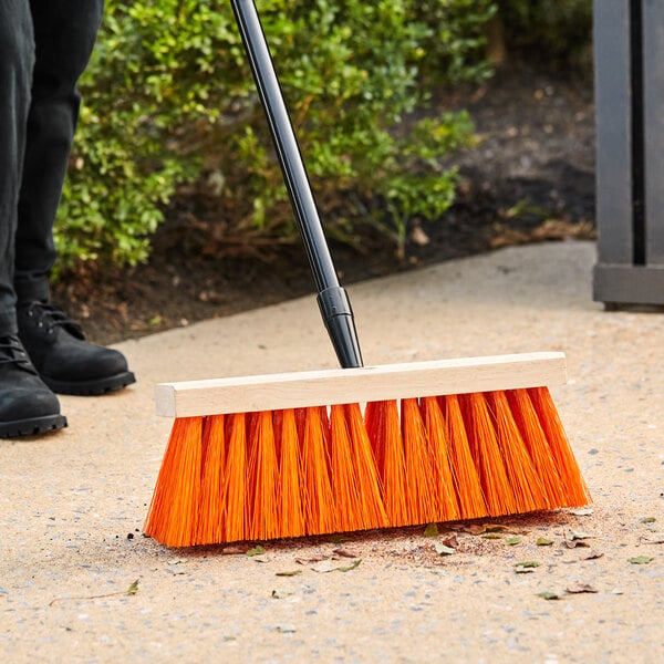 A person using a Lavex Wood Street Broom to sweep the sidewalk.