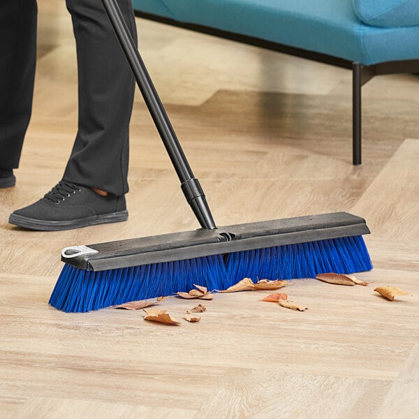 A person using a Lavex push broom to sweep a floor.