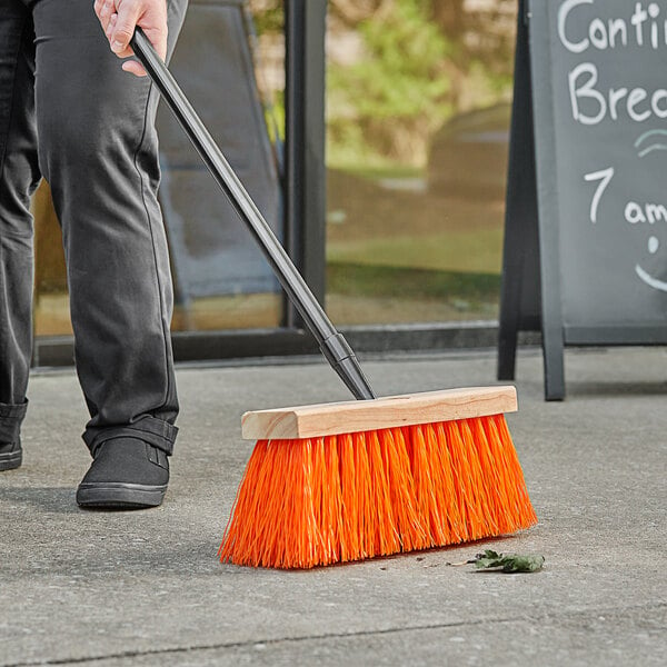 A person sweeping the sidewalk with a Lavex Heavy-Duty Wood Street Broom.