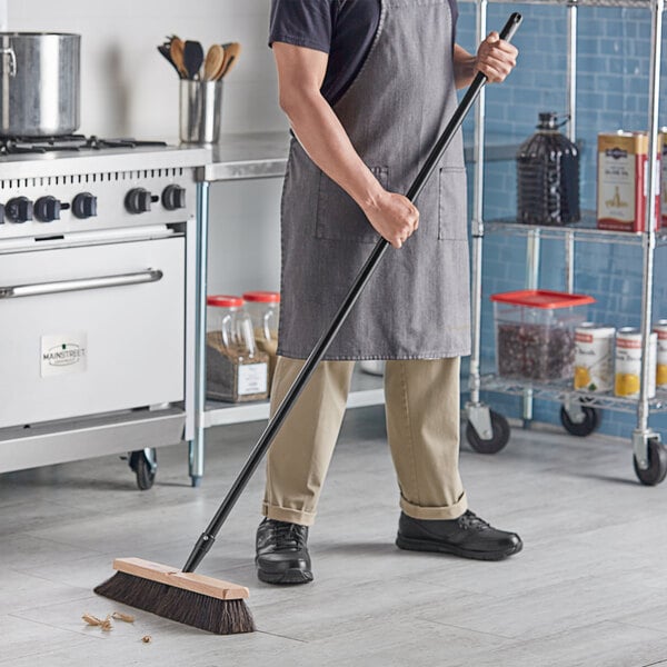 A man in an apron sweeping a floor with a Lavex wood push broom.