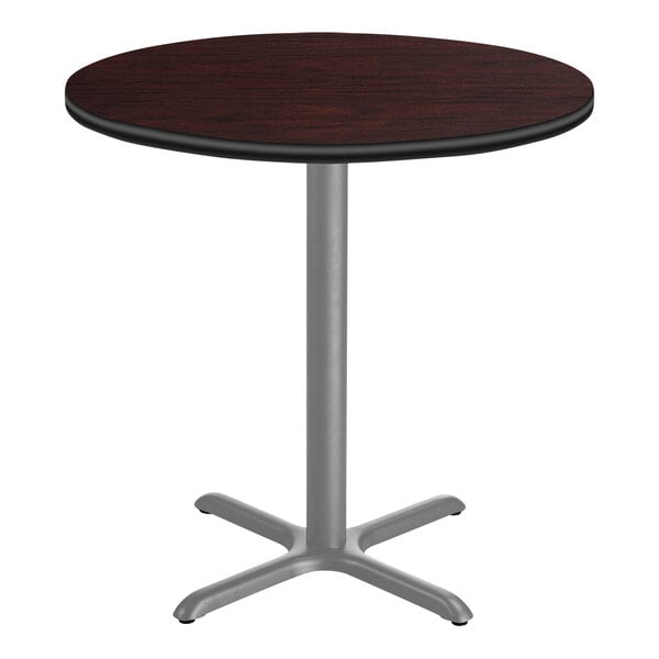 A National Public Seating round bar height table with a mahogany top and a gray metal base.