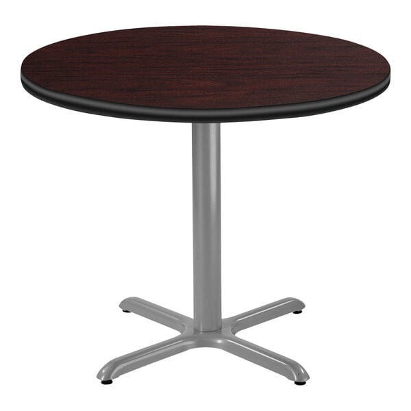 A National Public Seating round table with a mahogany wood top and X base with a gray frame.