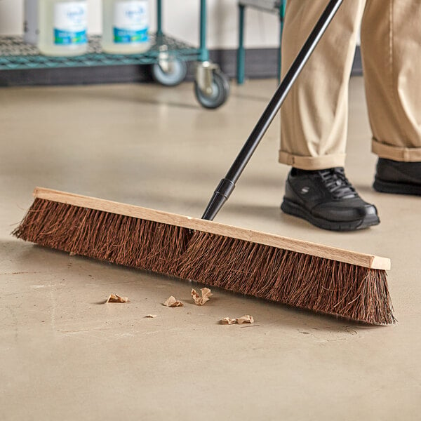 A person sweeping the floor with a Lavex wood push broom head.