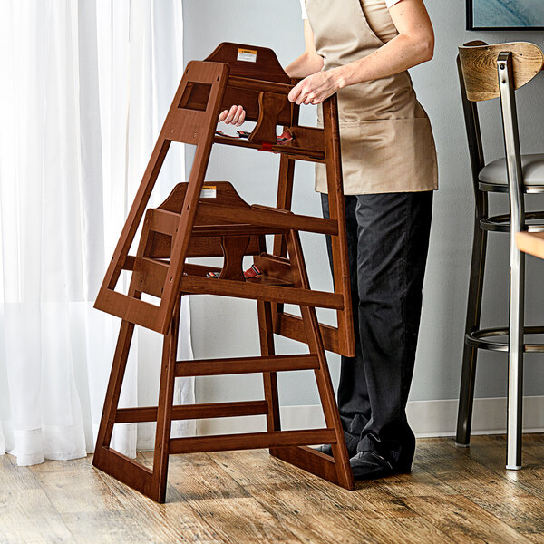 A woman standing next to a Lancaster Table & Seating wooden high chair on a table.