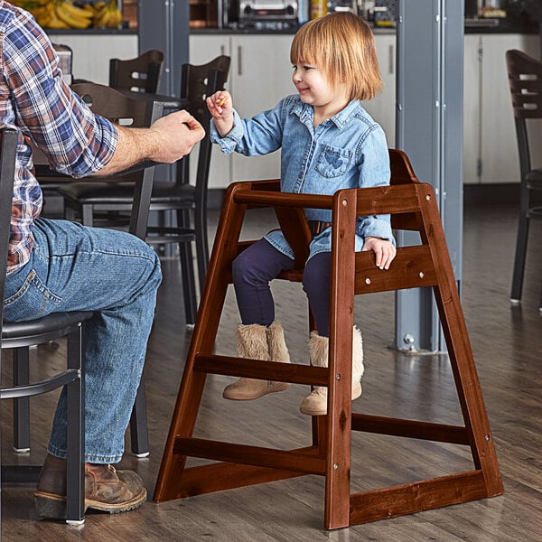 A child sitting in a Lancaster Table & Seating wooden high chair with a dark brown finish.